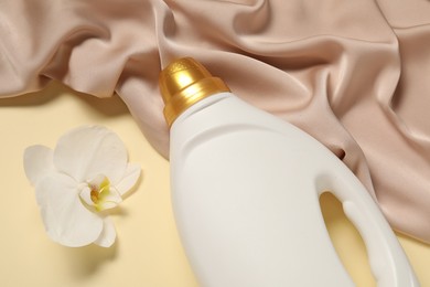 Photo of Bottle of fabric softener, orchid flower and color cloth on beige background, flat lay