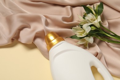 Photo of Bottle of fabric softener, flowers and color cloth on beige background, above view