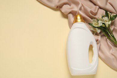 Photo of Bottle of fabric softener, flowers and color cloth on beige background, flat lay. Space for text