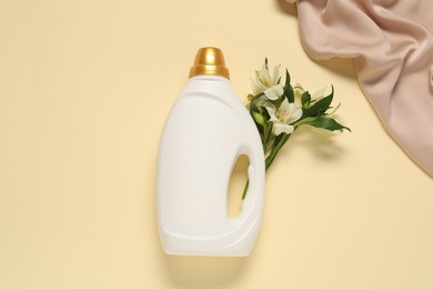 Photo of Bottle of fabric softener, flowers and color cloth on beige background, flat lay