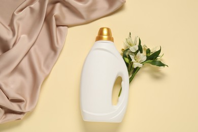 Photo of Bottle of fabric softener, flowers and color cloth on beige background, flat lay
