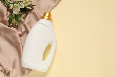 Photo of Bottle of fabric softener, flowers and color cloth on beige background, flat lay. Space for text