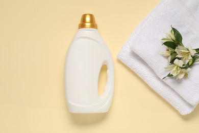 Photo of Bottle of fabric softener, flowers and terry towels on beige background, flat lay