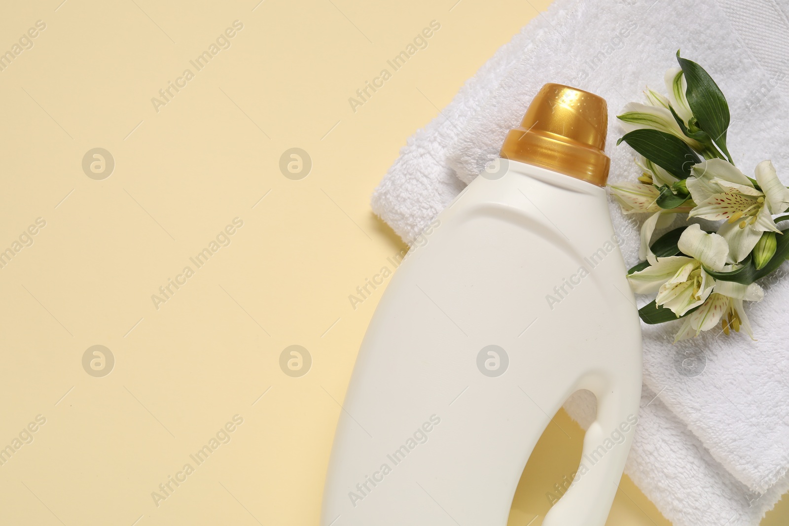 Bottle of fabric softener, flowers and terry towels on beige background, flat lay. Space for text Photo of Bottle of fabric softener, flowers and terry towels on beige background, flat lay. Space for text