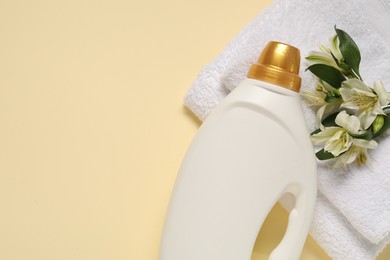 Photo of Bottle of fabric softener, flowers and terry towels on beige background, flat lay. Space for text