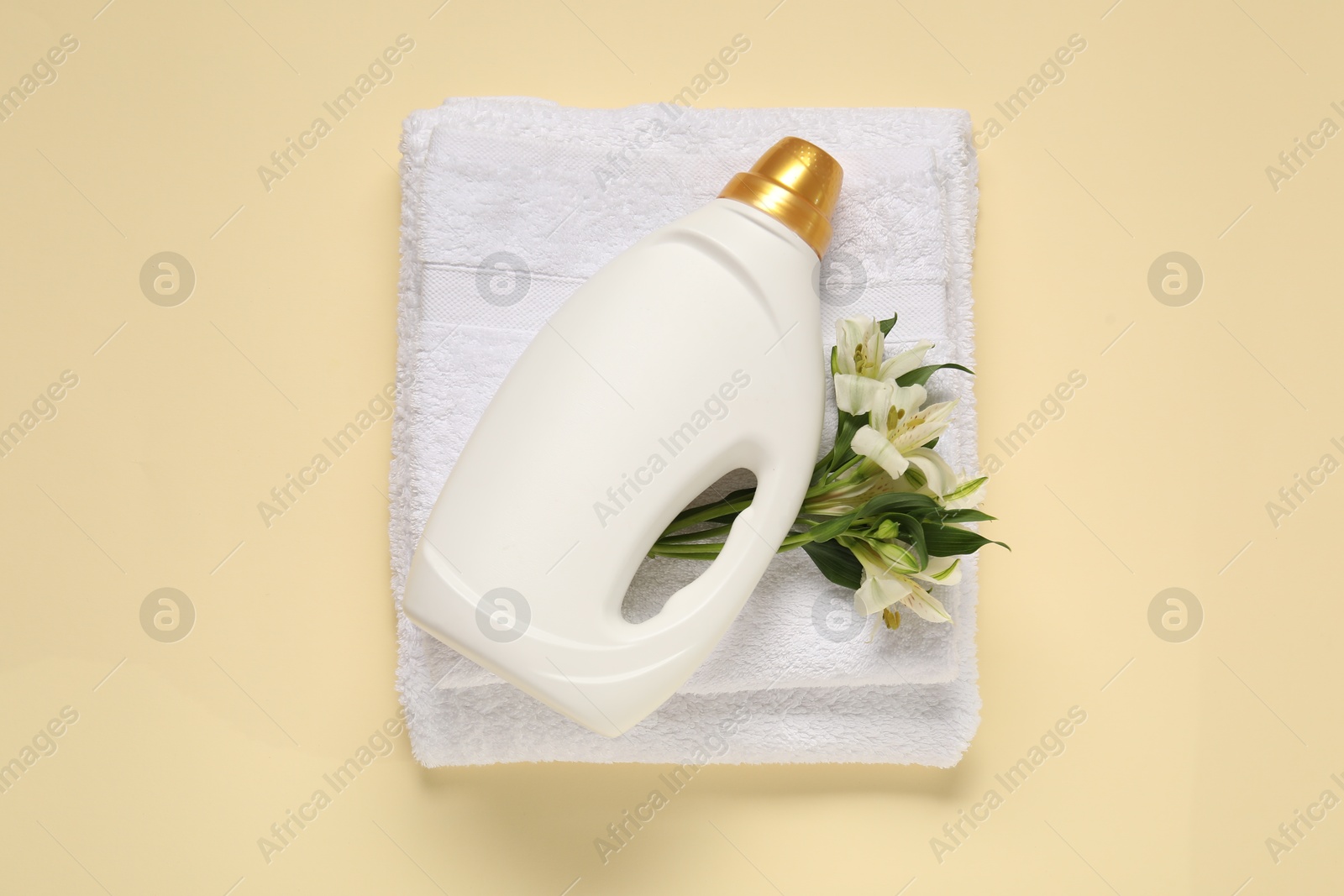 Bottle of fabric softener, flowers and terry towels on beige background, flat lay Photo of Bottle of fabric softener, flowers and terry towels on beige background, flat lay