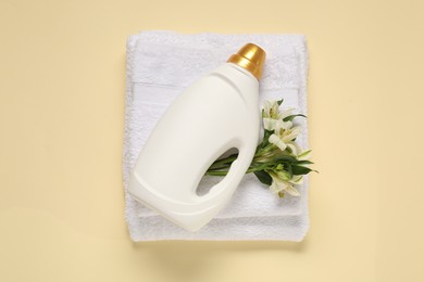 Photo of Bottle of fabric softener, flowers and terry towels on beige background, flat lay