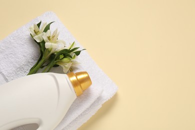 Photo of Bottle of fabric softener, flowers and terry towels on beige background, flat lay. Space for text