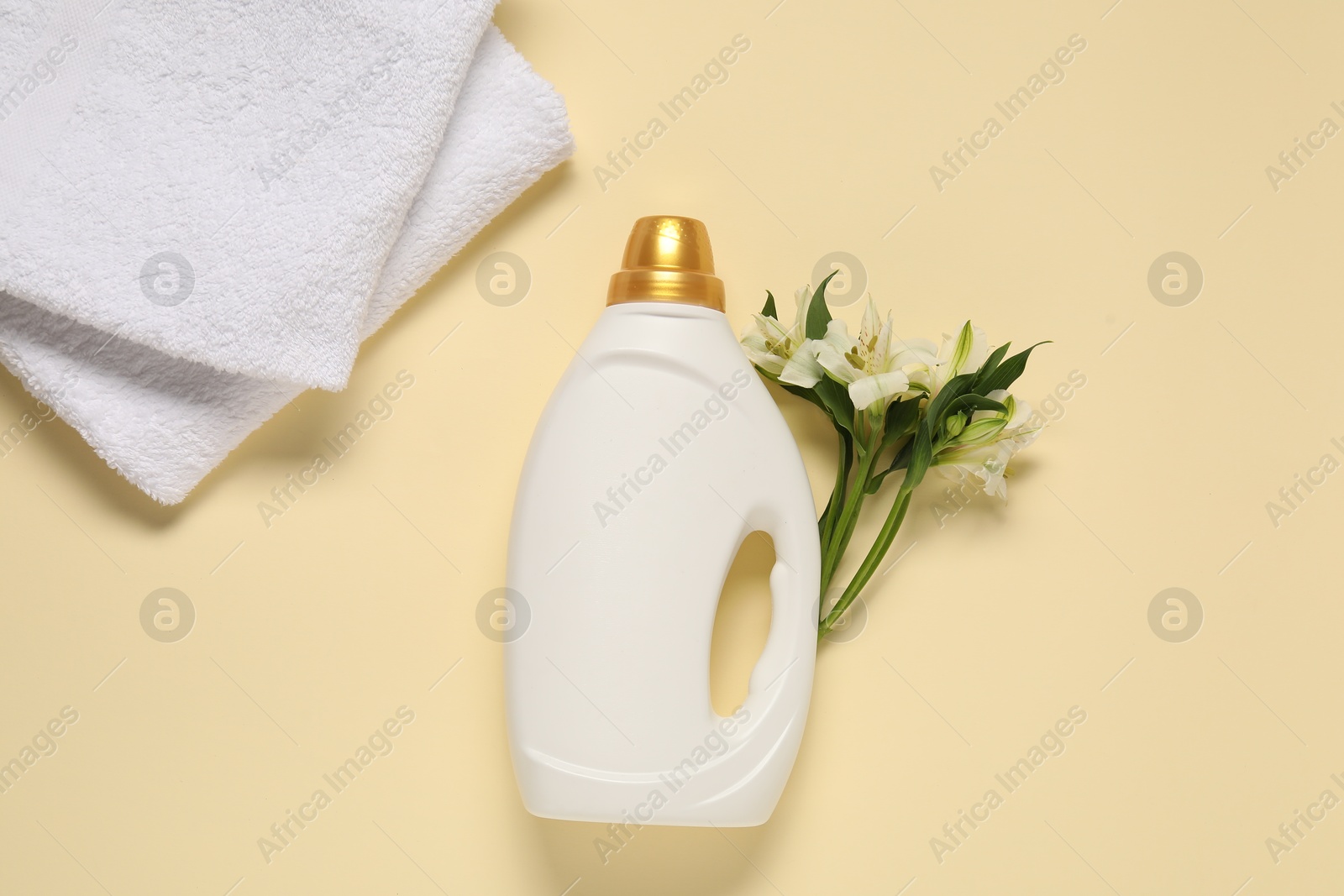 Bottle of fabric softener, flowers and terry towels on beige background, flat lay Photo of Bottle of fabric softener, flowers and terry towels on beige background, flat lay