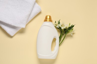 Photo of Bottle of fabric softener, flowers and terry towels on beige background, flat lay