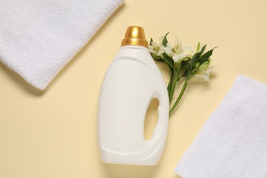 Photo of Bottle of fabric softener, flowers and terry towels on beige background, flat lay