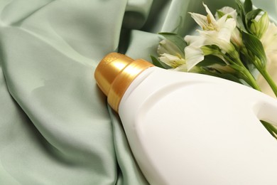 Photo of Bottle of fabric softener and flowers on green cloth, above view