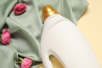 Photo of Bottle of fabric softener, flowers and green cloth on beige background, above view