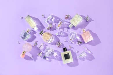 Photo of Flat lay composition with perfume bottles and lilac flowers on violet background