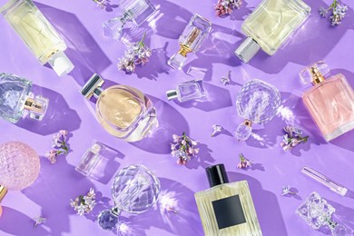 Photo of Flat lay composition with perfume bottles and lilac flowers on violet background