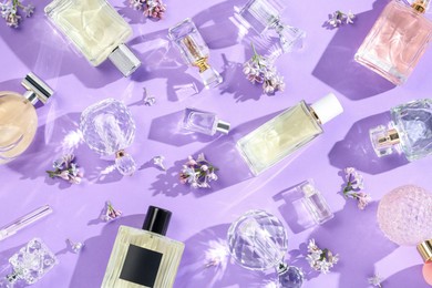 Photo of Flat lay composition with perfume bottles and lilac flowers on violet background