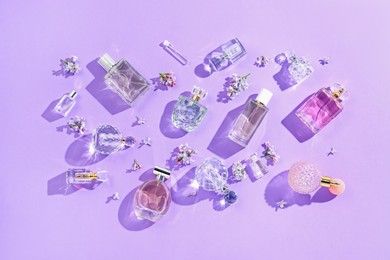 Photo of Flat lay composition with perfume bottles and lilac flowers on violet background