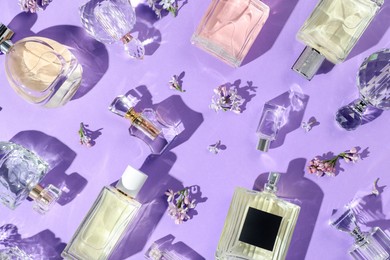 Photo of Flat lay composition with perfume bottles and lilac flowers on violet background