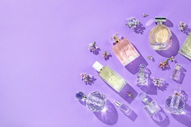 Photo of Flat lay composition with perfume bottles and lilac flowers on violet background. Space for text