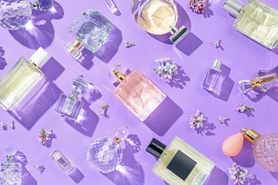 Photo of Flat lay composition with perfume bottles and lilac flowers on violet background