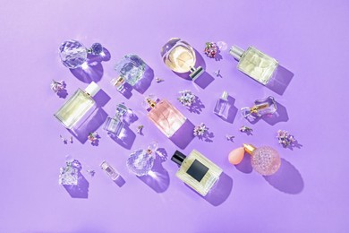 Photo of Flat lay composition with perfume bottles and lilac flowers on violet background