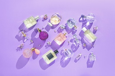 Photo of Flat lay composition with perfume bottles and lilac flowers on violet background