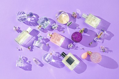 Photo of Flat lay composition with perfume bottles and lilac flowers on violet background
