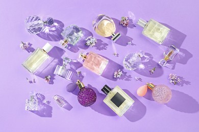 Photo of Flat lay composition with perfume bottles and lilac flowers on violet background