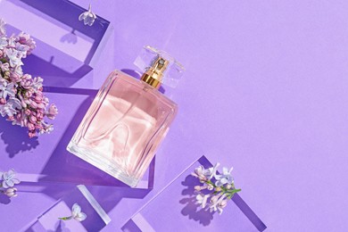 Photo of Flat lay composition with bottle of perfume and lilac flowers on violet background. Space for text