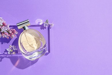 Photo of Bottle of perfume and lilac flowers on violet background, flat lay. Space for text
