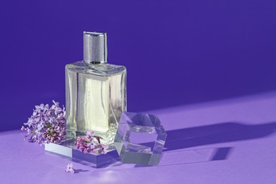 Photo of Stylish presentation of perfume bottle and lilac flowers on purple background, closeup. Space for text