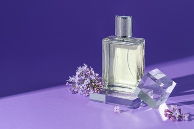 Photo of Stylish presentation of perfume bottle and lilac flowers on purple background, closeup. Space for text