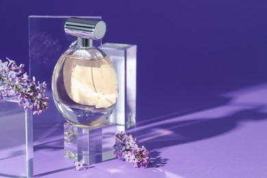 Photo of Stylish presentation of perfume bottle and lilac flowers on purple background, closeup. Space for text