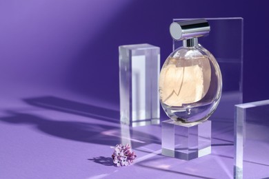 Photo of Stylish presentation of perfume bottle and lilac flowers on purple background, closeup. Space for text