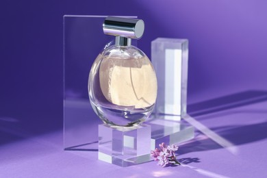 Photo of Stylish presentation of perfume bottle and lilac flowers on purple background, closeup