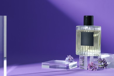 Photo of Stylish presentation of perfume bottle and lilac flowers on purple background, closeup. Space for text