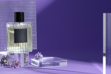 Photo of Stylish presentation of perfume bottle and lilac flowers on purple background, closeup. Space for text