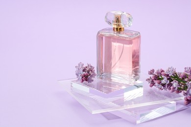 Photo of Stylish presentation of perfume bottle and lilac flowers on violet background, closeup. Space for text