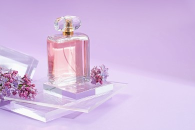 Photo of Stylish presentation of perfume bottle and lilac flowers on violet gradient background, closeup. Space for text
