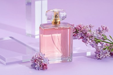 Photo of Stylish presentation of perfume bottle and lilac flowers on violet background, closeup