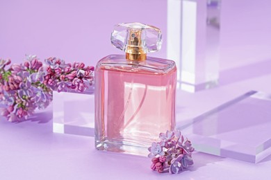Photo of Stylish presentation of perfume bottle and lilac flowers on violet background, closeup
