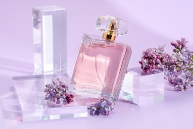 Photo of Stylish presentation of perfume bottle and lilac flowers on violet background, closeup