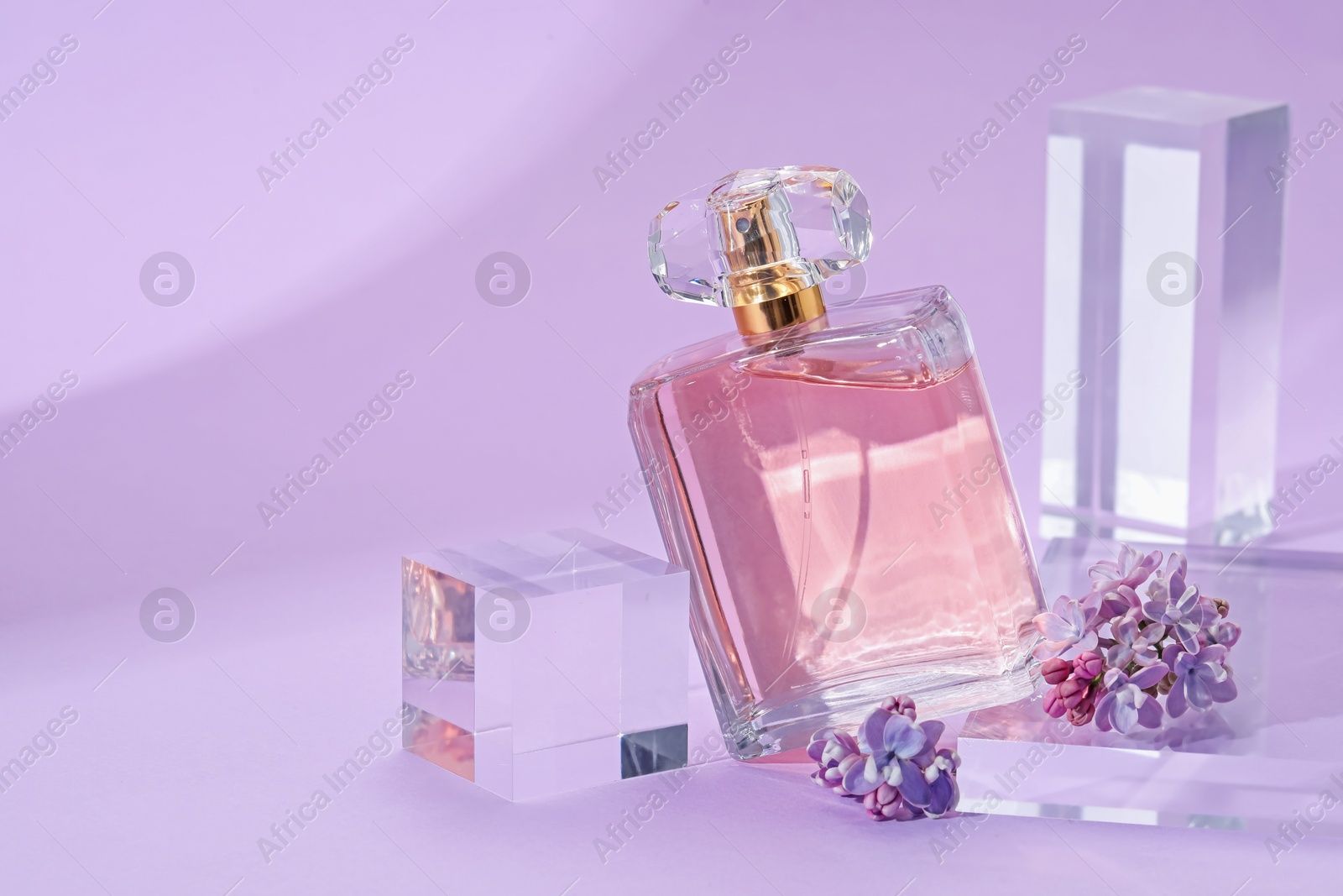 Photo of Stylish presentation of perfume bottle and lilac flowers on violet background, closeup. Space for text