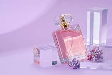 Photo of Stylish presentation of perfume bottle and lilac flowers on violet background, closeup. Space for text