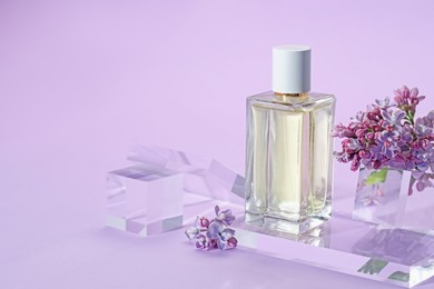 Photo of Stylish presentation of perfume bottle and lilac flowers on violet background, closeup. Space for text