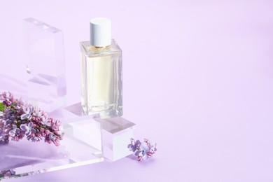 Photo of Stylish presentation of perfume bottle and lilac flowers on violet background, closeup. Space for text