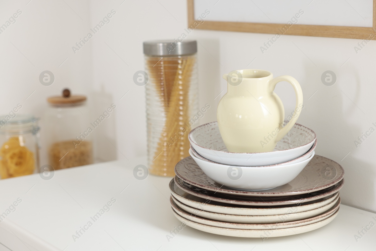 Clean ceramic jug, bowls and plates on white table in kitchen, space for text Photo of Clean ceramic jug, bowls and plates on white table in kitchen, space for text