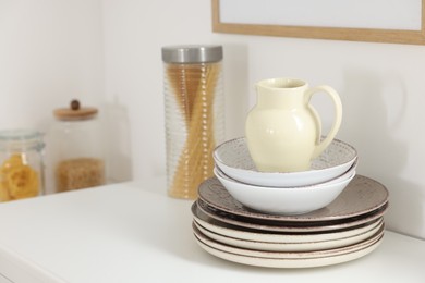 Photo of Clean ceramic jug, bowls and plates on white table in kitchen, space for text