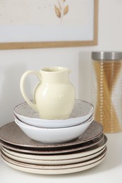 Photo of Clean ceramic jug, bowls and plates on white table in kitchen