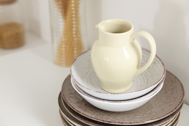 Photo of Clean ceramic jug, bowls and plates on white table in kitchen, closeup. Space for text